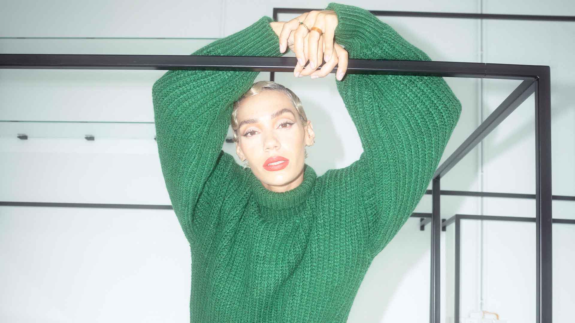 mimabooysen_im_gruenen_Pullover_Haende_ueber_Stange_gelegt_guckt_in_die_Kamera